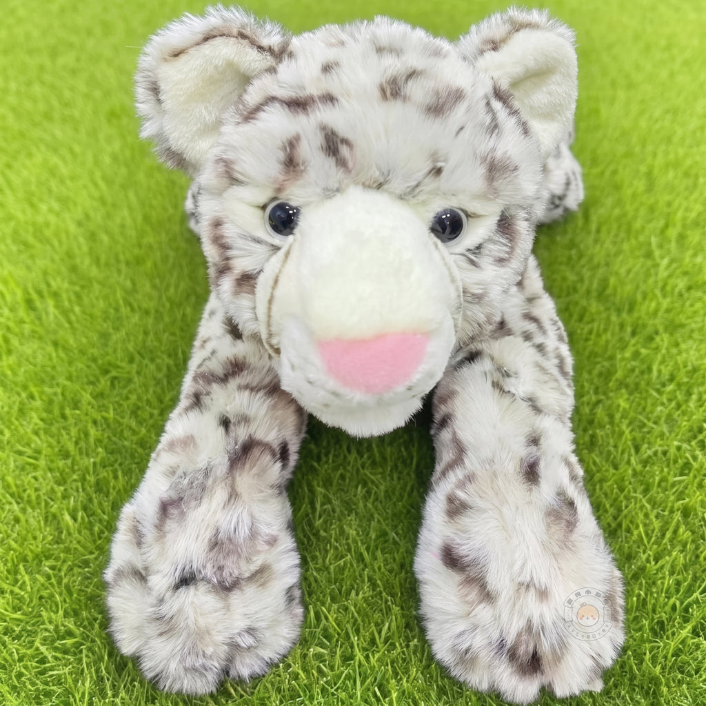 芝生の上で前足を伸ばして伏せるユキヒョウぬいぐるみ。つぶらな瞳と愛らしいピンクの鼻先がチャームポイント