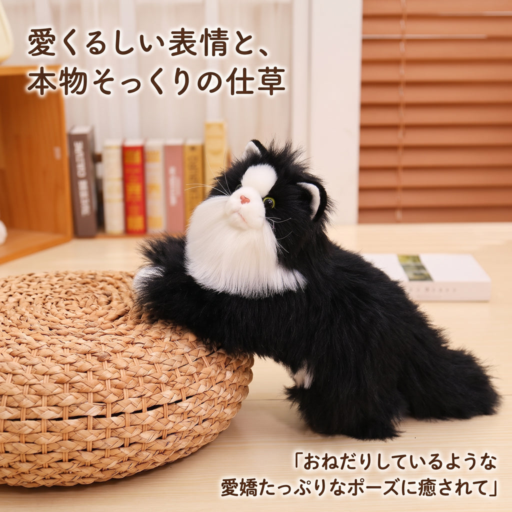 ラタンのクッションにあごや前足を乗せておねだりするような仕草を見せるリアルハチワレ猫ぬいぐるみ