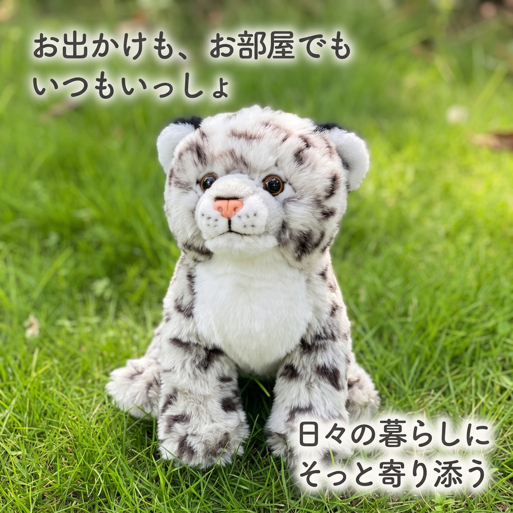緑の芝生の上で前足を揃えてお座りするリアルユキヒョウぬいぐるみ。日々の暮らしにそっと寄り添う小さな相棒