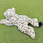 芝生に寝そべるユキヒョウぬいぐるみの後ろ姿。背中に広がる美しい豹柄模様と先端が黒い太いしっぽ