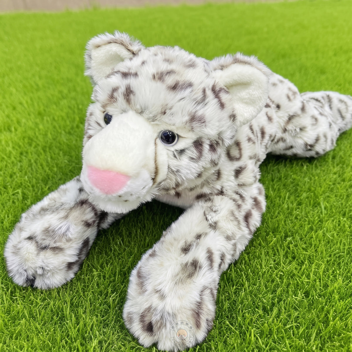 芝生の上から見上げてくるリアルなユキヒョウぬいぐるみ。ふっくらとした大きな前足と思わず撫でたくなる上質な肌触り