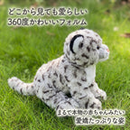 芝生の上で横を向くユキヒョウぬいぐるみのサイドビュー。まるで本物の動物の赤ちゃんのような愛嬌たっぷりな姿