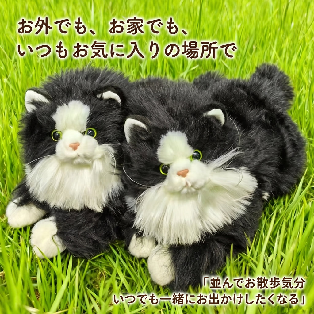 緑の芝生の上に並んで寝そべる2匹のリアルなハチワレ猫ぬいぐるみ。お外でもお家でも一緒にお出かけしたくなる愛らしい姿