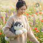 花畑の中で腕に抱えられるリアルなアラスカンマラミュートの子犬ぬいぐるみ